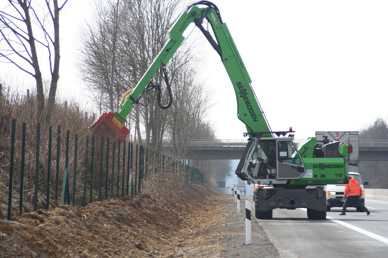 Forestry mulcher head on an excavator boom clearing brush along an embankment
